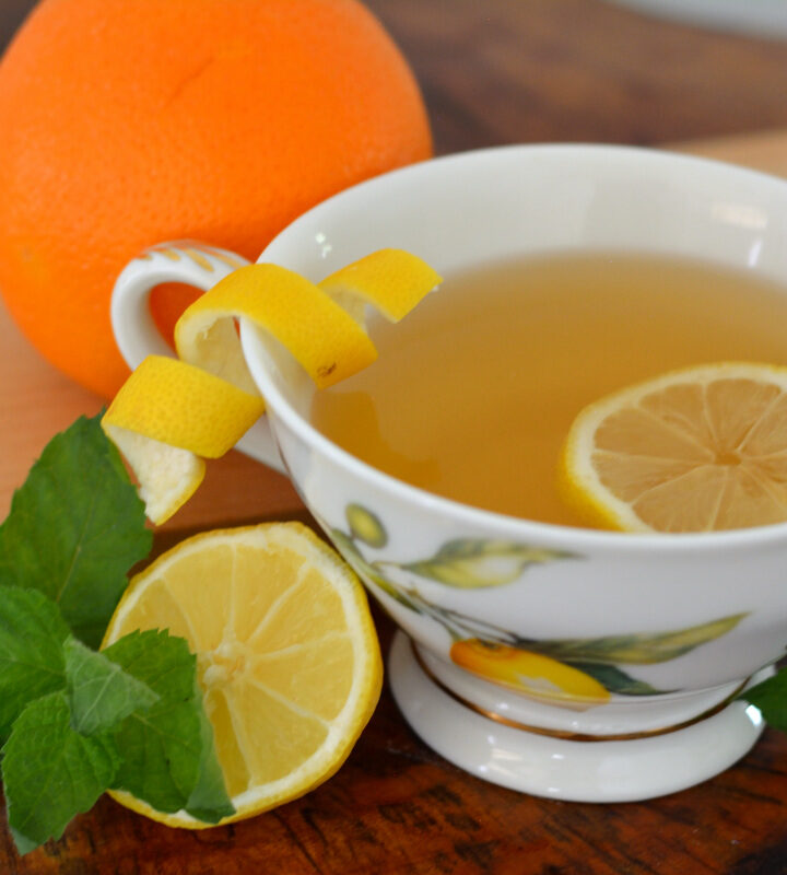 Tea cup with lemon slice, lemon peel, and fresh mint on wooden table.
