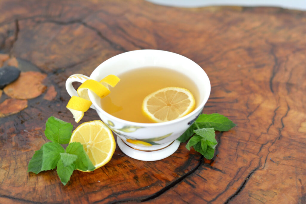 Tea cup with unique additives to add to tea such as lemon slice, lemon peel, and fresh mint on wooden table.