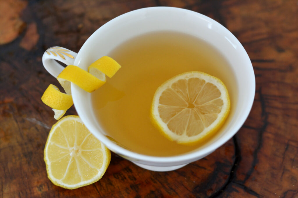 Tea cup with unique additives to add to tea such as lemon slice and lemon peel on wooden table.
